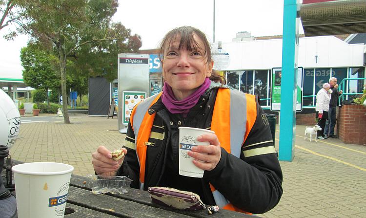 Sharon smiles while drinking tea and eating a pastry at ferrybridge services