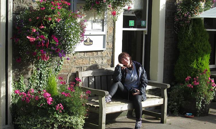 Sharon strikes a cute pose on a bench surrounded by flowers in Hawes