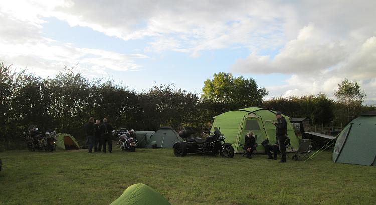Tents, bikes, trikes, cars and people just hanging out chatting in the field