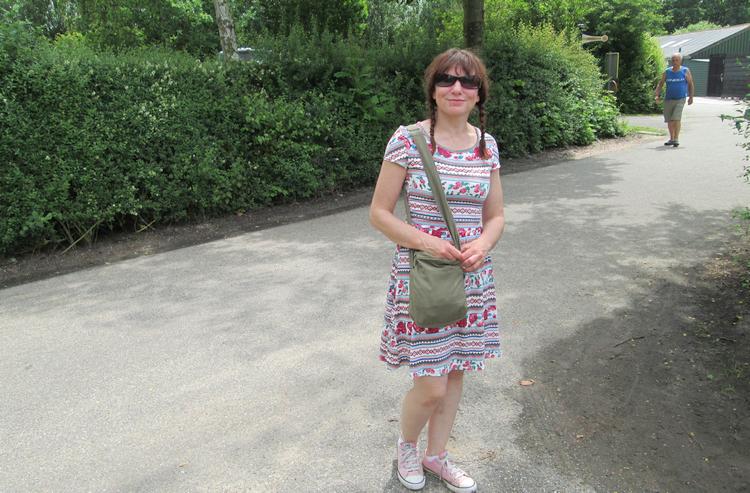 Sharon stands in her summer dress and shades, smiling
