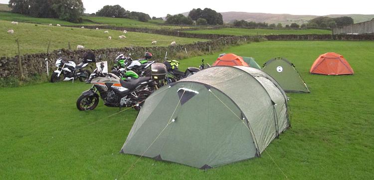 A group of motorcycles and tents on a field in the countryside