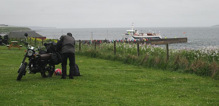 A Motorcyclist finished his packing while in the distance tourists board the foot ferry to The Orkneys