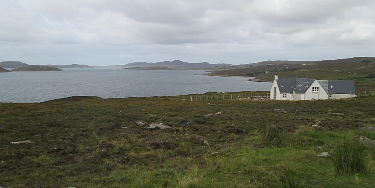 A modern highland house painted traditionally white, all alone set against a broad sea loch
