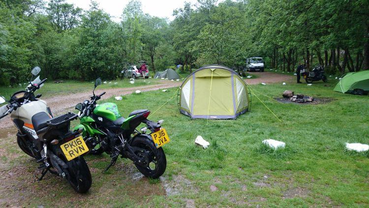 The motorcycles are at the wet and tree filled campsite as the tent is put up