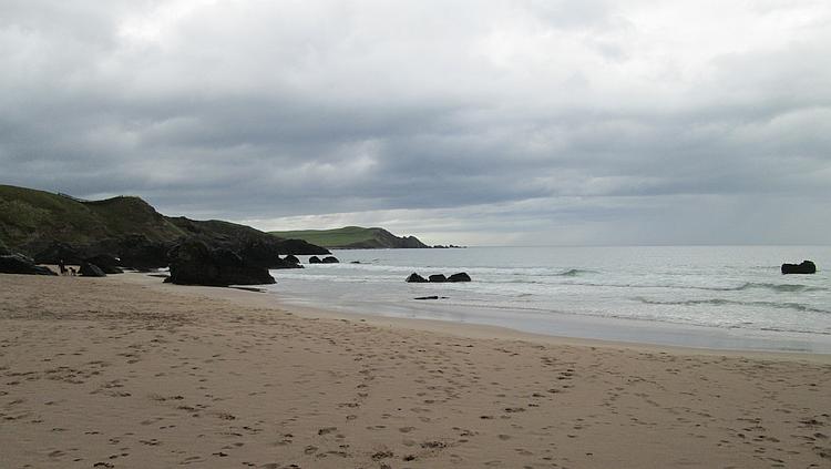 Rugged rock lead down to a sandy beach in the rain at Durness