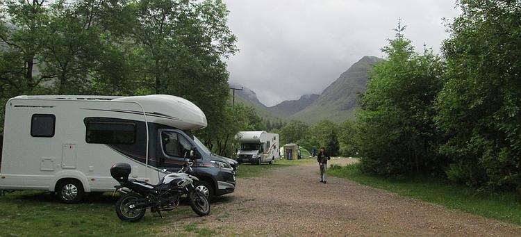 A campervan and motorcycles set against the dramatic and steep hillsides of the Glencoe valley