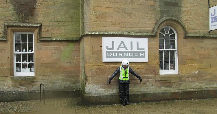 Sharon looks forlorn in her bike gear under the Dornoch Jail sign