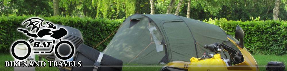 A motorcycle parked in front of a tent on a pleasant green campsite