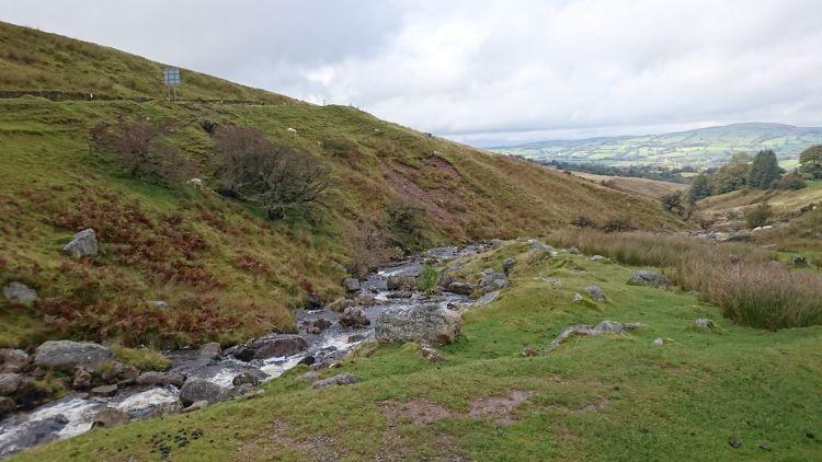 Looking down the cut of a stream we see over countryside and towns from the pass