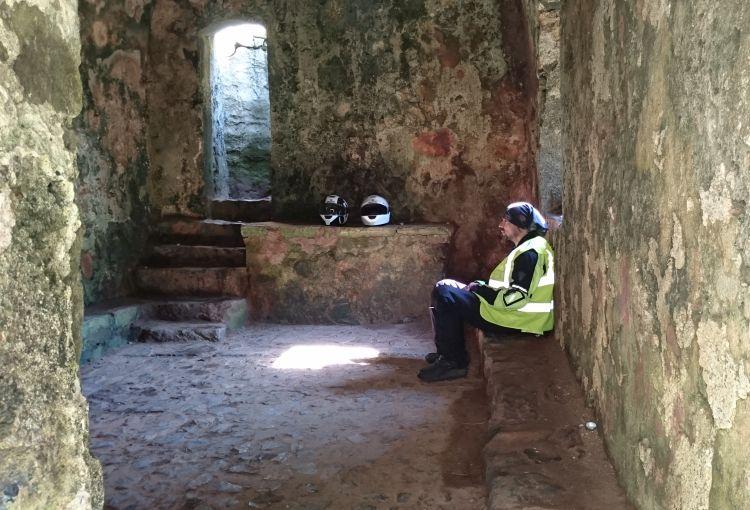 Ren sits within the stone chapel, a small sparse room with open windows and doors