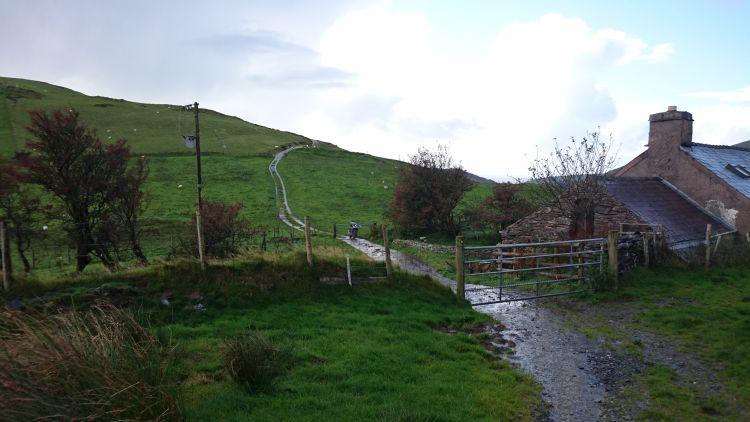 The motorcycle looks forlorn at the end of the road up against a gate in the middle of nowhere