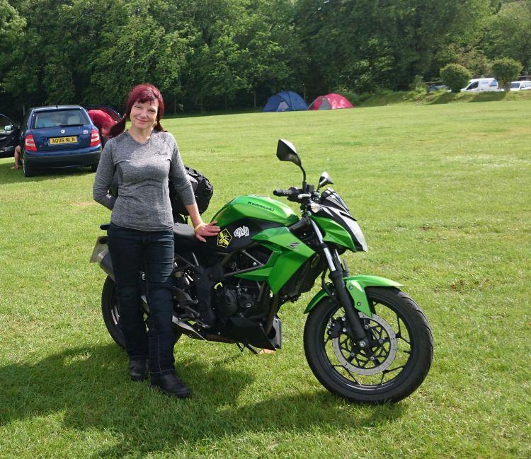Sharon stands next to her bike proudly pointing out the bee sticker on the side of her Kawasaki