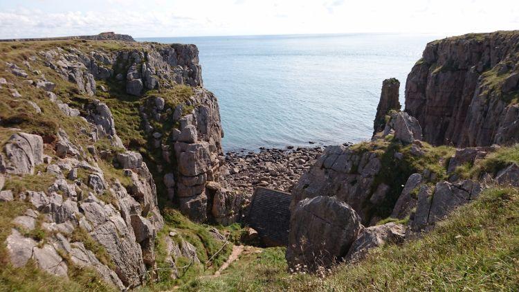 Between craggy rocky cliffs we can see the sea and the roof of a very small building