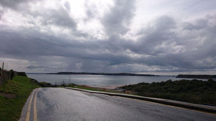 Dark skies and a wet road lead down to a view across the calm bay at Tenby