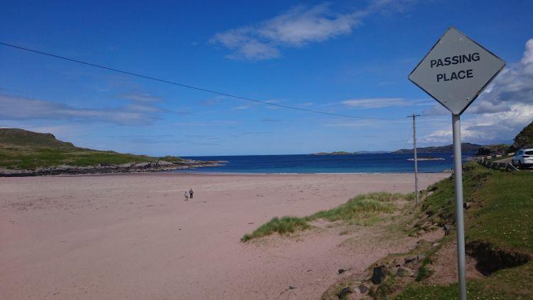 A broad sandy beach in a cove, all bathed in blue skies and sunshine.