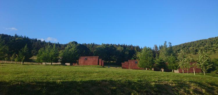 Several camping pods in a large field with trees covering the nearby hillsides