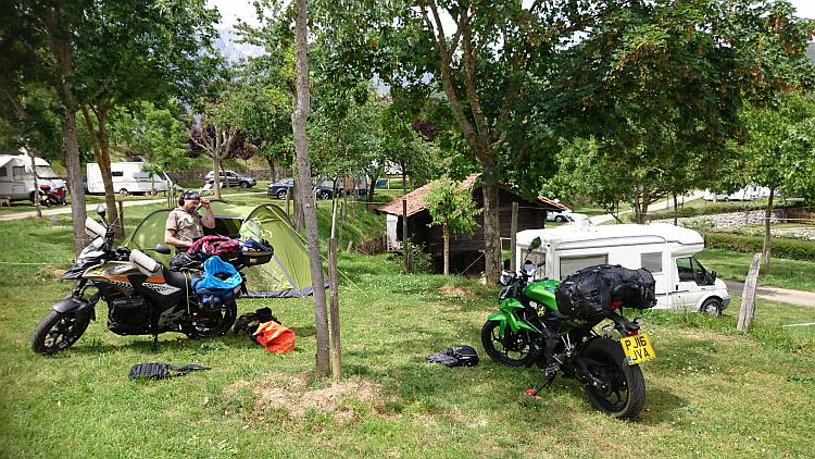 Ren is next to the tent and the bike finishing pitching in the sun at the wooded campsite