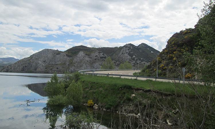 A road is visible to the side of the reservoir, curving around and exciting