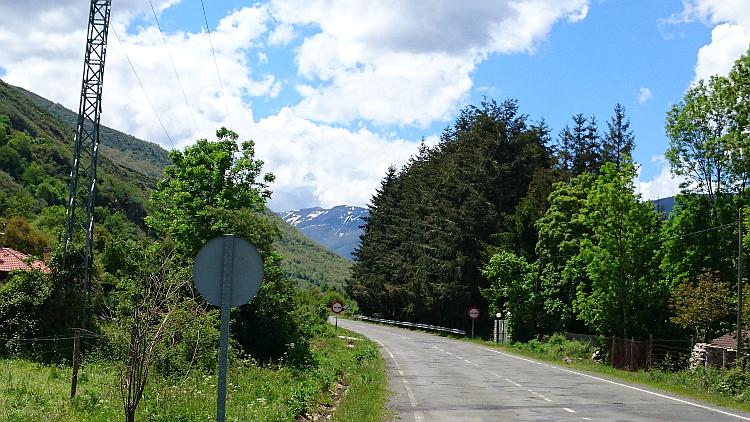 A road makes it's way between steep hills with snow capped mountains in the distance