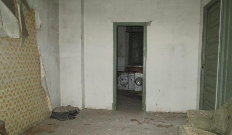 Inside a ruin wallpaper peels off the walls amidst dust and dirt and an old washing machine