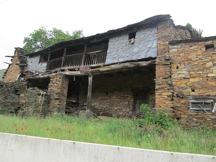 A stone and wood house that's falling apart and ramshackle by the side of the road