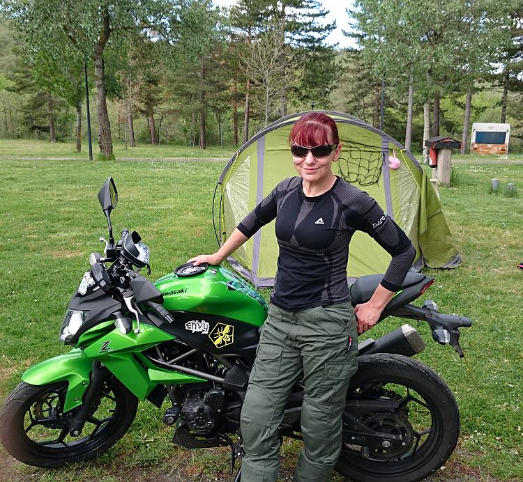 Sharon poses by her bike in front of the tent on a tree filled campsite