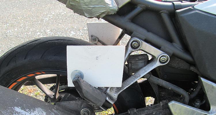 A small square piece of white painted wood bolted on to the footrest hangar of Ren's 500