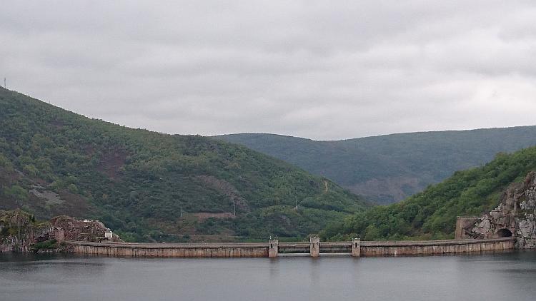 The waters suddenly stop at a beige concrete barrier, this is the top of the dam that forms the reservoir