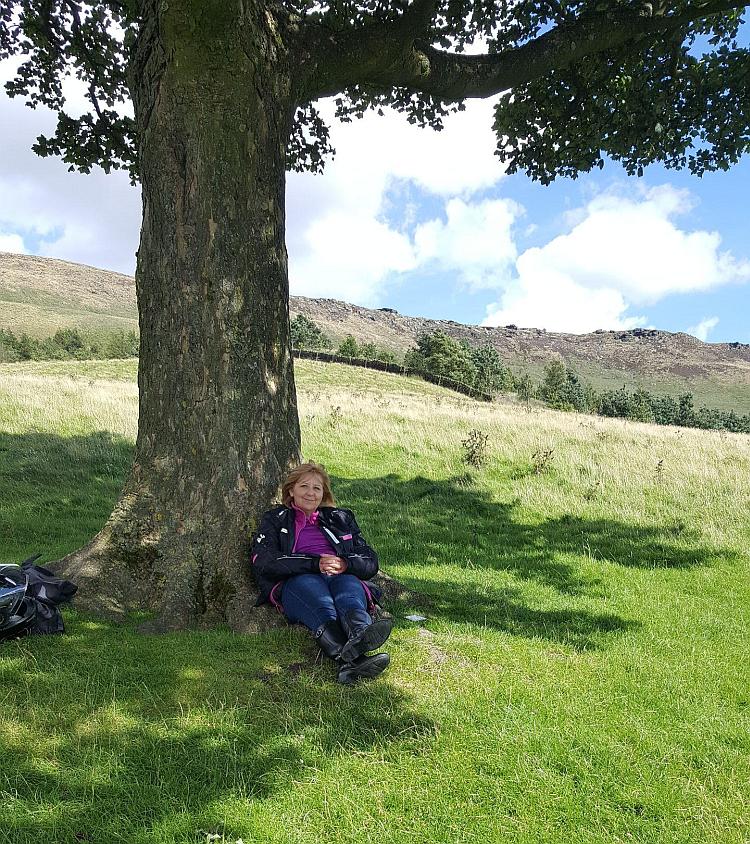 Paula is resting in the shade of a tree on a warm day, but she has her bike gear on