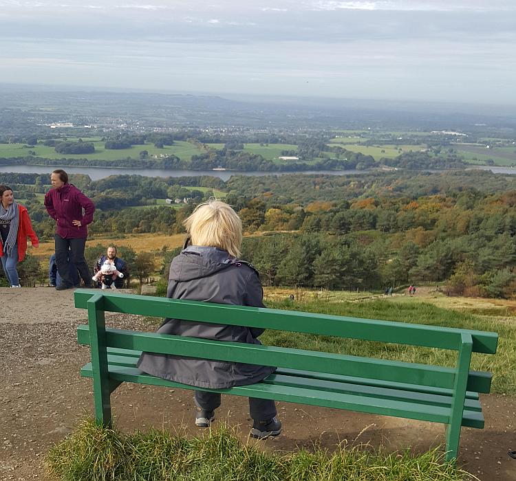 Paula is sat on a bench overlooking a vast plain on a hazy day