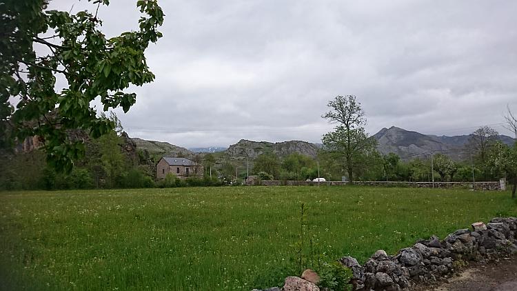 Looking out over a broad field and flat green valley in the background grey rocky hills