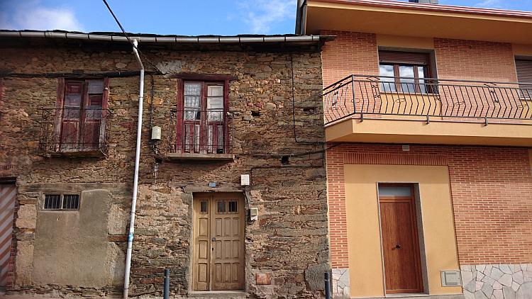 A stone house with bent and aged guttering and windows next to a sharp clean modern property