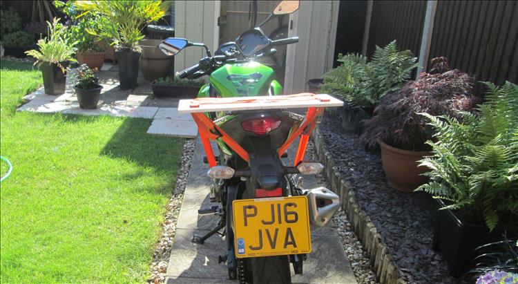 A plank of wood about 2 feet long strapped to the rear seat of the Z250SL with ratchet straps
