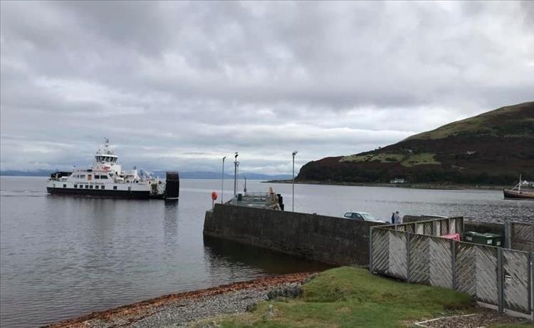 A small car ferry in the small port at Lochranza under grey skies but calm waters