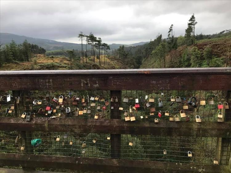 Rugged scenery behind a drige with wire mesh. On the mesh are hundreds of love locks
