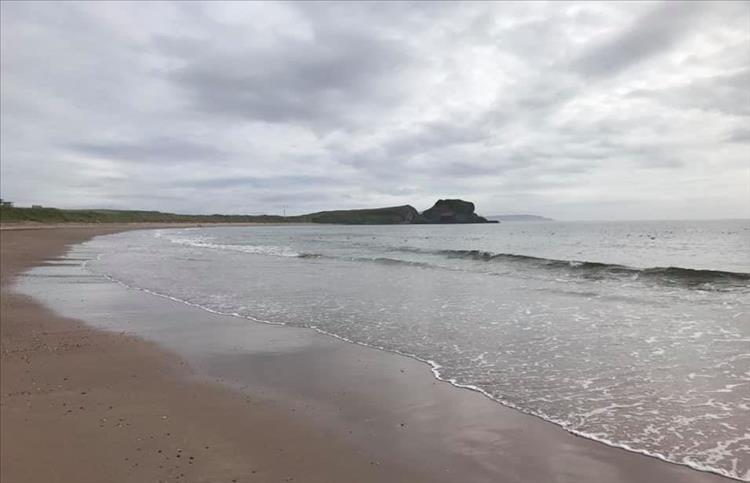 A large sandy beach, rocky outcrops and small waves at Southend, Mull of Kintyre