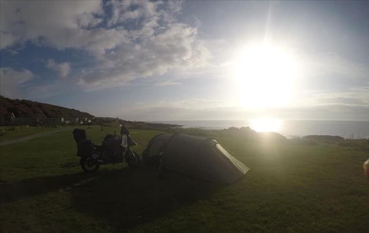 The tent and the bike at the campsite. Beautiful scenery, bright sun in light cloud and the sea