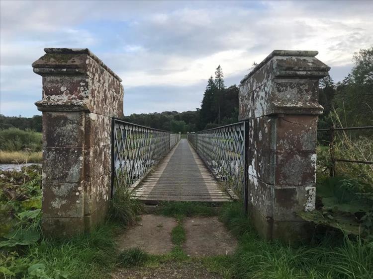 A steel trellis footbridge with wooden floor crosses a river