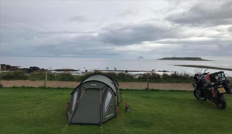 Andy's tent and motorcycle looking out over the waters on a grey yet beautiful scene