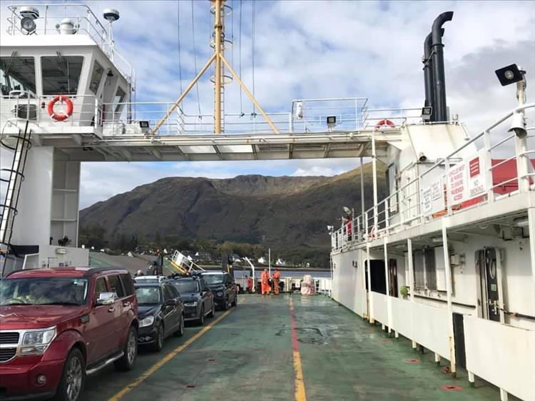 The ferry with a it's bridge and a selection of cars on the green painted deck