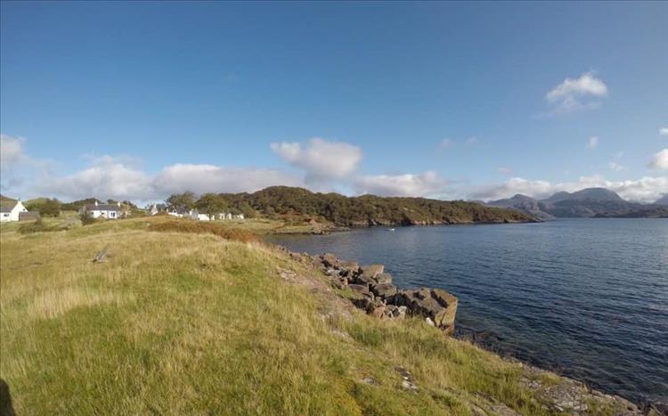 The calm sea and sunshine next to small white highland houses and thick lush grasses