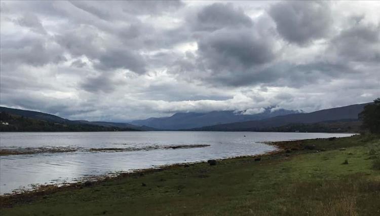 Thick heavy clouds, grassy shoreline and mountains in the mist all at Loch Eil near Fort William