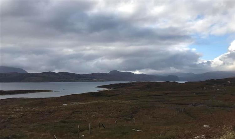 A board hardy moor leads down to the loch shore, with mountains in the grey skies beyond