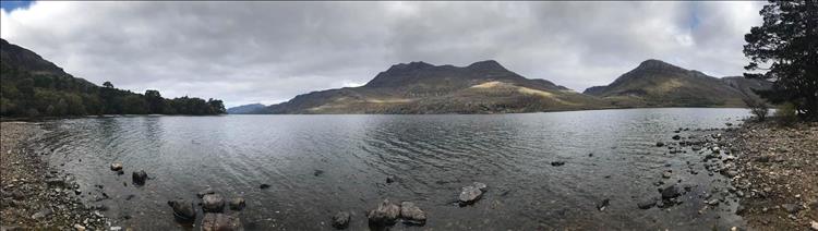 Wide andlge shot of a loch with the angular hills and mountains beyond the stoney beach