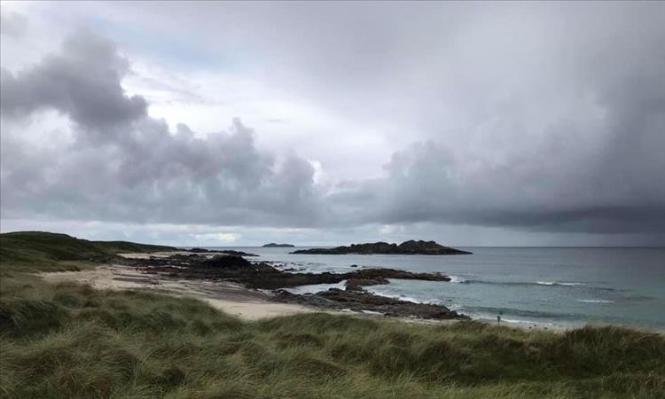 Sands, hardy grasses, rocks and the sea under turgid skies of Iona