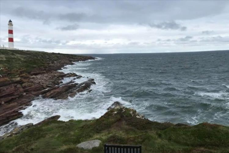 A white and red lighthouse standing onto of a rocky promontory and the North sea