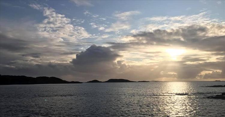 Hazy blue skies, darker clouds, sun and the calm waters off West Scotland