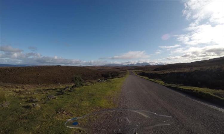 A narrow lane winds across hardy moorlands with a clump of mountains in the far distance