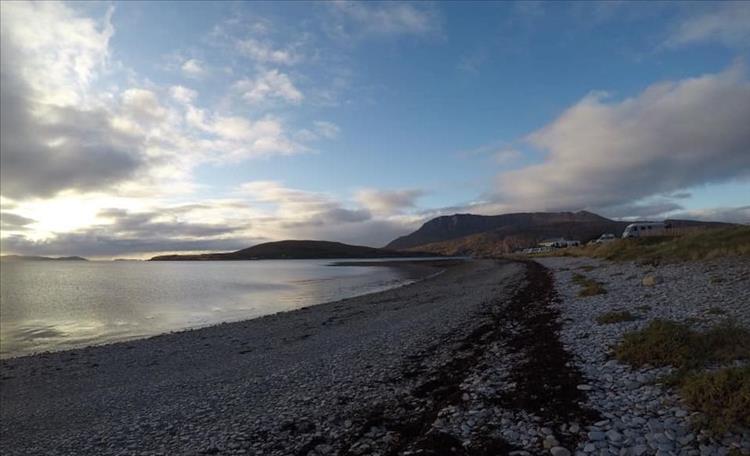 A logn pebble beach curves away into the distance, just inland we can see a campervan or two