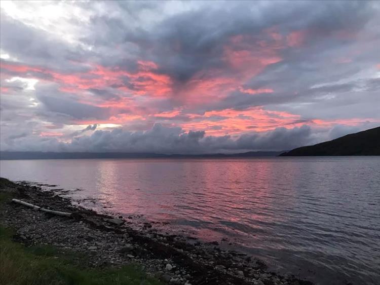 From the shore the clouds are orange-red as the sun sets over the waters